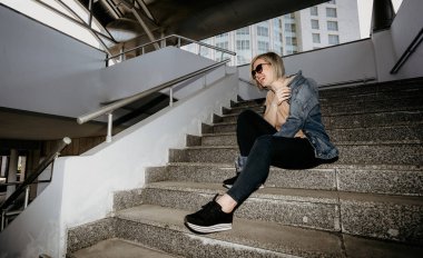 Güzel sarışın merdivenlerde otururken gülüyor. Büyük şehirde modern kadın