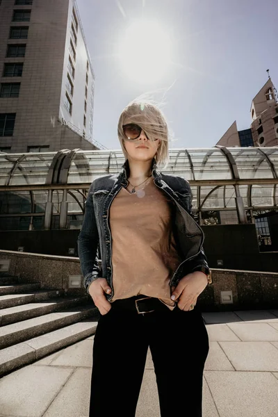Красивая блондинка на фоне современного города в солнечную ветреную погоду смотрит в камеру. Портрет современной женщины — стоковое фото