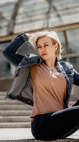 Beautiful blonde takes off her glasses. Sits on the city steps. Loneliness in the modern city — Stock Photo, Image