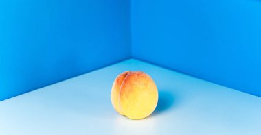 Mavi bir arka plan üzerinde beyaz bir masada olgun şeftali. Masa köşesi