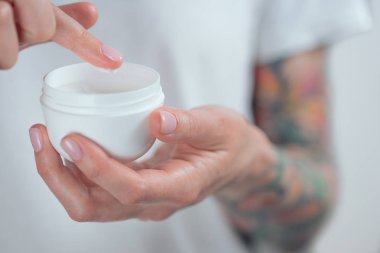 Kadın dövmeli eller bir kavanoz krema tutuyor. Beyaz krem bir damla ile Parmak