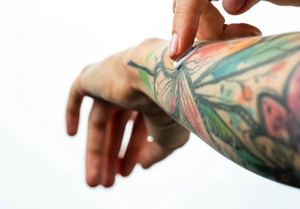 Le mani tatuate femminili tengono un barattolo di crema. Le dita applicano la crema a pelle. Da vicino. — Foto Stock