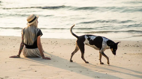 Uma menina de chapéu de palha senta-se na praia da manhã. Menina moderna em férias — Fotografia de Stock