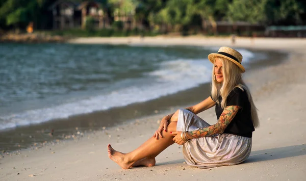 Een meisje in een stro hoed zit op het ochtend strand. Modern meisje op vakantie — Stockfoto