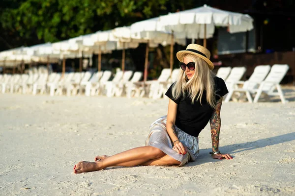 Девушка в соломенной шляпе сидит на утреннем пляже. Современная девушка в отпуске — стоковое фото