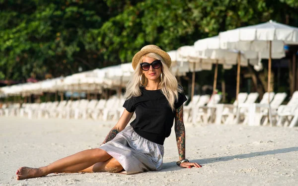 Egy lány egy szalmakalapot ül a reggeli strandon. Modern lány nyaralni — Stock Fotó