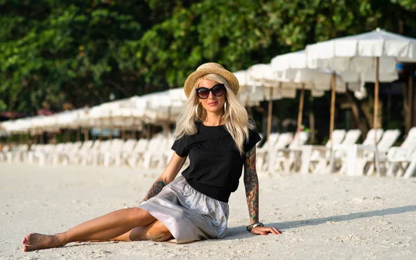 Een meisje in een stro hoed zit op het ochtend strand. Modern meisje op vakantie — Stockfoto