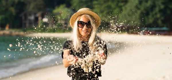 Het strand zand wordt wakker van de handen van een mooie blonde in zonnebrillen. Strandvakantie. Portret van een modern meisje. — Stockfoto