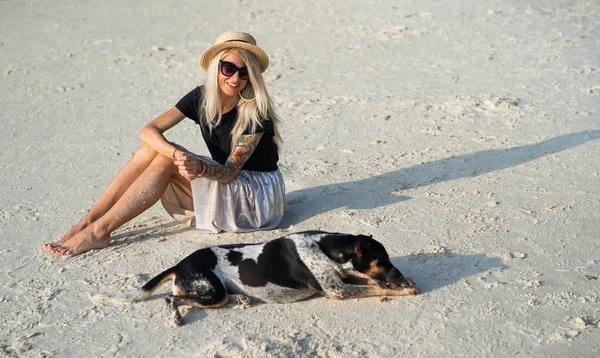 Egy lány egy szalmakalapot ül a reggeli strandon. Modern lány nyaralni — Stock Fotó