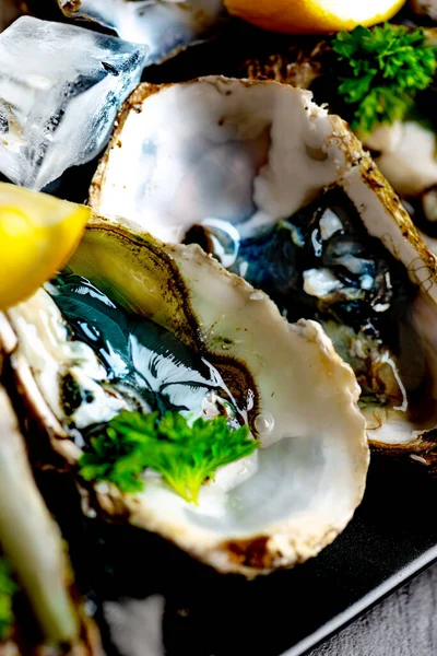 Raw opened oysters on plate with ice, lemon and parsley