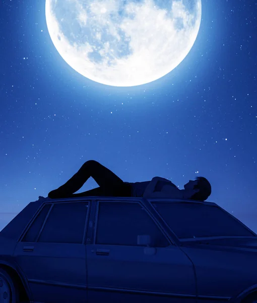 Man lying down on the car roof and looking to the moon - Stock Image -  Everypixel