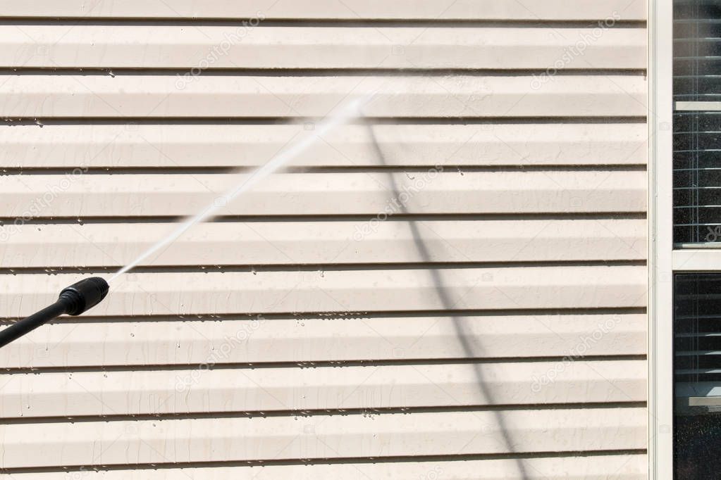 Power washing. House wall vinyl siding cleaning with high pressure water jet.