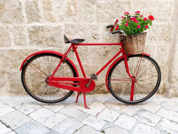 Czerwony rower z koszem kwiatów na starej kamiennej ścianie na włoskim — Zdjęcie stockowe