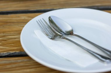 çatal ve kaşık ahşap masa üzerinde beyaz plaka ile