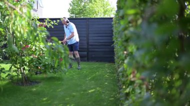 Bir adam bahçesindeki çimleri makineyle kesiyor.