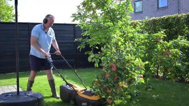 Bir adam bahçesindeki çimleri makineyle kesiyor.