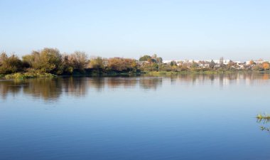 Nehirli sonbahar manzarası, berrak bir nehirde mavi gökyüzü yansıması.