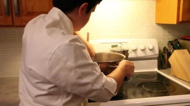 Stovetop üzerinde büyük bir buharlı pot karıştırma bir şefin ceketli bir kişinin görünümü Kapat 