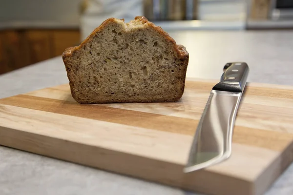 On a wooden cutting board, a sharp knife has sliced homemade baked banana bread