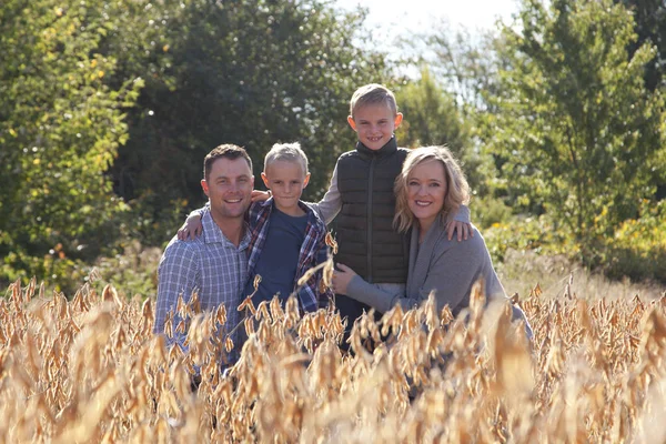 Beautiful blond family, with a mother and father and two boys, crouches in a field for a family photo