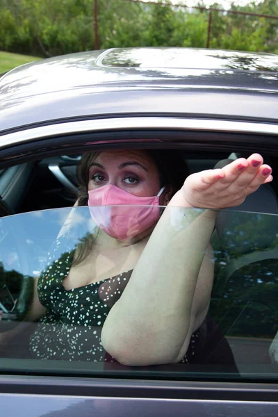 person wearing a mask with their hand out their car window picking something up at a distance