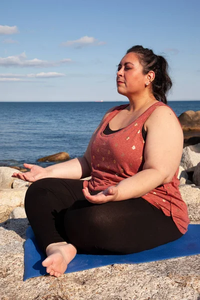 peaceful woman invites spirituality or mindfulness while sitting on a rocky coastline