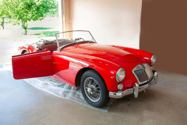 beautiful top down sports car in bright red on a plastic tarp in someone\'s garage that has been greatly loved
