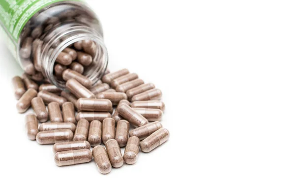 Birkaç yeşil çay özü kapsülbeyaz bir yüzeye dökülen bir plastik şişe. Sağlık kavramı.