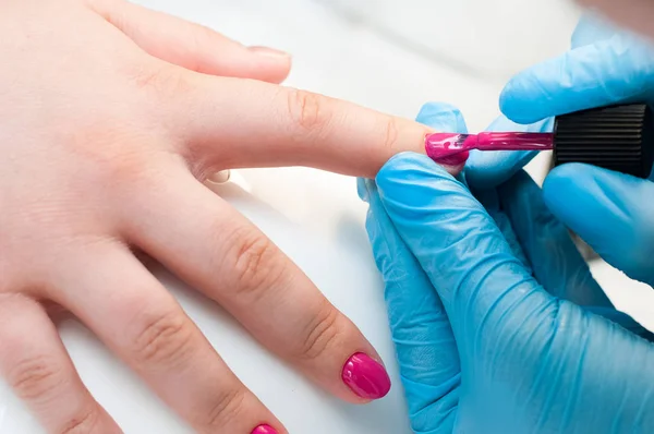 Manicure nail paint pink color. Nail care. Closeup of beautiful woman hands getting manicure in spa salon. Female manicurist cleaning cuticle with professional manicure. Cosmetic procedure.
