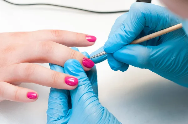 Manicure nail paint pink color. Nail care. Closeup of beautiful woman hands getting manicure in spa salon. Female manicurist cleaning cuticle with professional manicure. Cosmetic procedure.