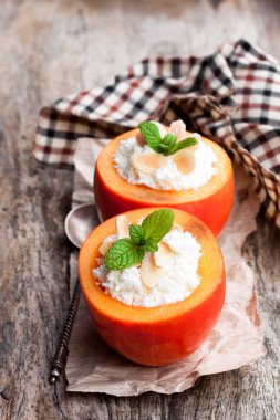 Sweet  persimmons stuffed with cottage cheese and almonds on wooden table  clipart