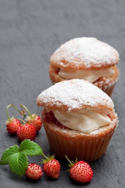 Siyah taş zemin üzerine beyaz krem ve yabani çilek ile doldurulmuş cupcakes 