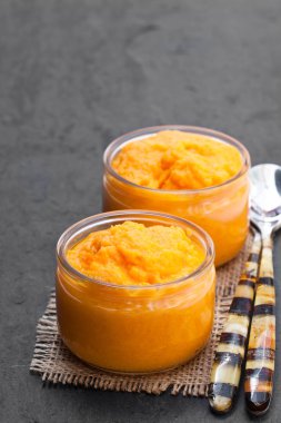 Siyah taş zemin üzerine cam kavanozlara turuncu sebze püresi 