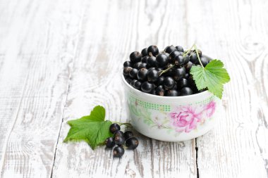 Beyaz ahşap masa üzerinde seramik kase taze siyah frenk üzümü 