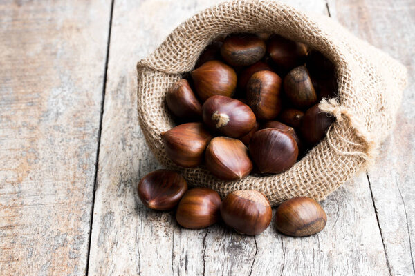 Свежие каштаны в мешочке на старом деревянном столе
 