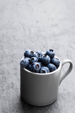 Siyah taş arka planda taze olgun yaban mersini dolu fincan 