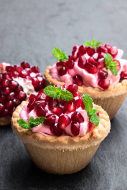 Siyah taş arka planda pembe krem ve nar tohumları ile mini tarts 