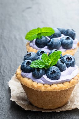 Siyah taş arka plan üzerinde mavi krem ve taze yaban mersini ile Mini tart 