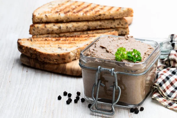 Paté fresco en frasco de vidrio con pan tostado en mesa de madera blanca — Foto de Stock