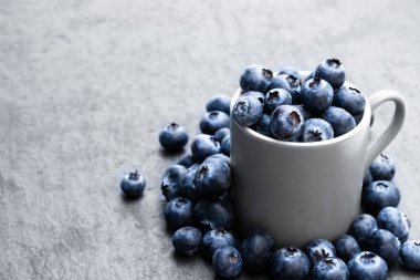 Siyah taş arka planda taze olgun yaban mersini dolu fincan 