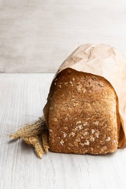 Beyaz ahşap masa üzerinde kağıt torba içinde yulaf gevreği ile ev yapımı kepekli ekmek 