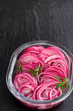 Salamura edilmiş kırmızı soğan halkaları siyah taş arka planda cam kasede. 