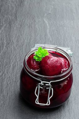 Ev yapımı bebek pancar kökü ve siyah taş arka planda cam muhafaza kavanozu. 