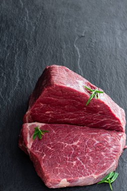 Koyu bir taş tahtada otlu çiğ biftek. 
