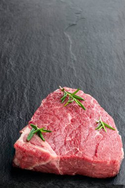 Koyu bir taş tahtada otlu çiğ biftek. 
