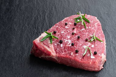 Koyu bir taş tahtada otlu çiğ biftek. 