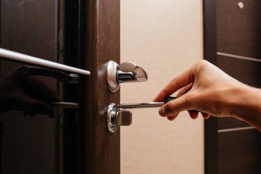 Bir adam odanın kapısındaki kilidi tornavidayla onarıyor. Mekanizmaların kendi kendilerine onarılması.