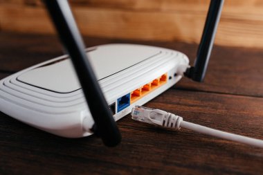 Karanlık ahşap bir masadaki yönlendiriciye bağlanmamış bir LAN kablosu. Yüksek hızlı wi-fi internet eksikliği. 
