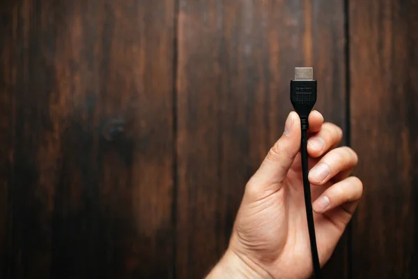 Muž drží v rukou černý HDMI kabel na tmavém dřevěném pozadí. Různá rozhraní připojující zařízení — Stock fotografie