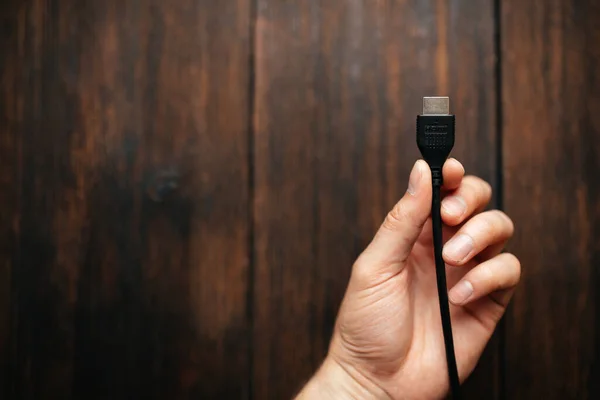 Siyah HDMI kablosunu elinde tutan bir adam koyu ahşap bir arka planda. Aygıtlara bağlanan farklı arayüzler